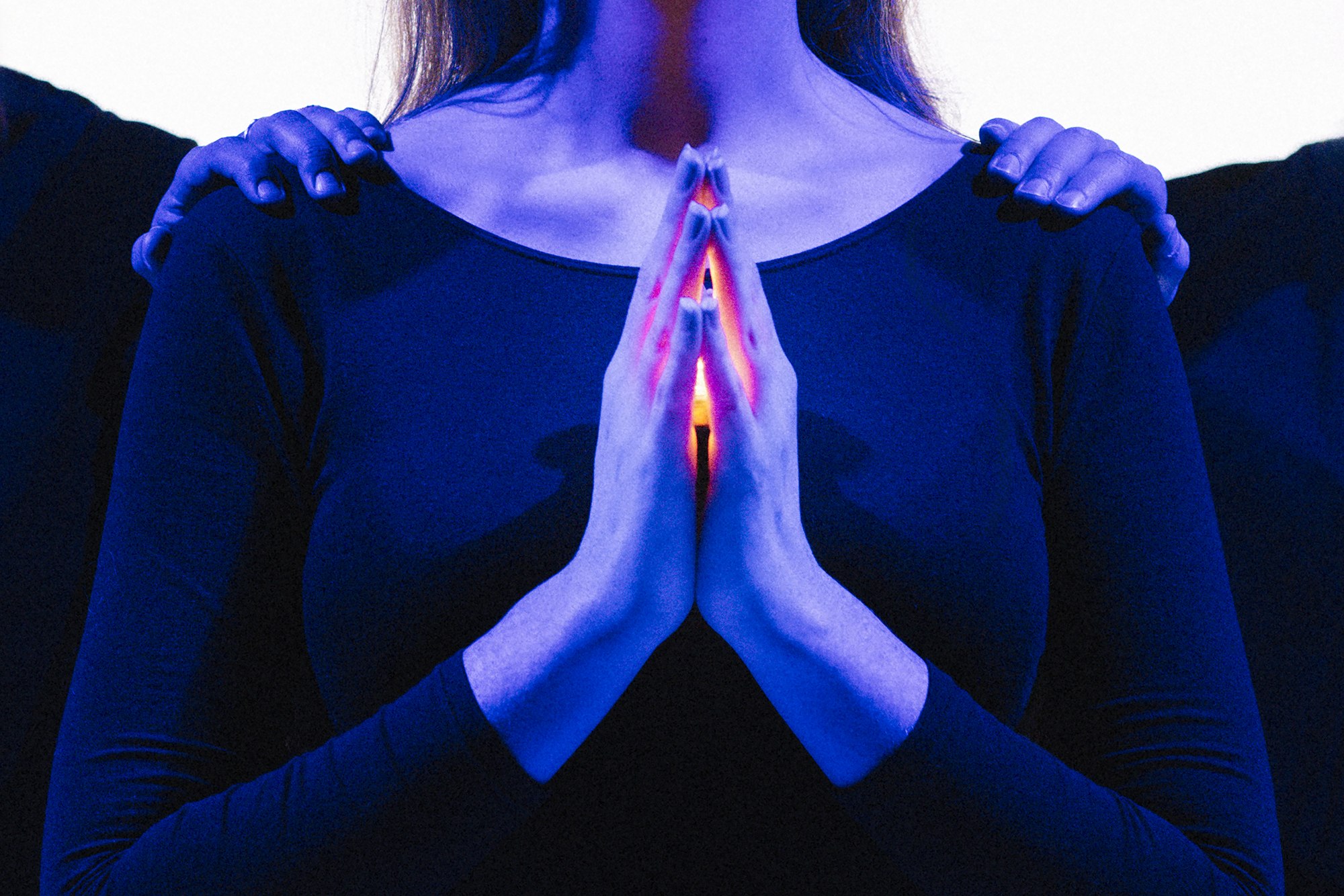 A woman bathed in blue light holds her hands together in prayer. A glow emanates from them.